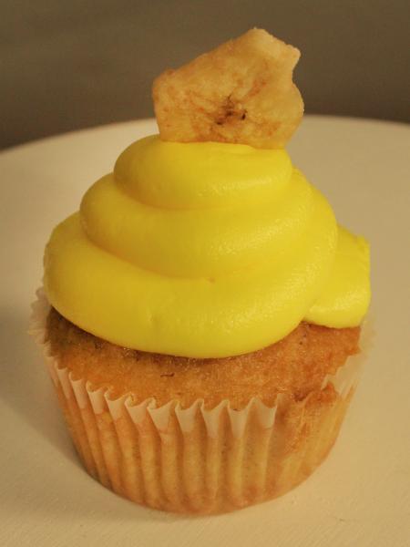 A delicious banana cupcake with yellow icing and a banana chip on top.