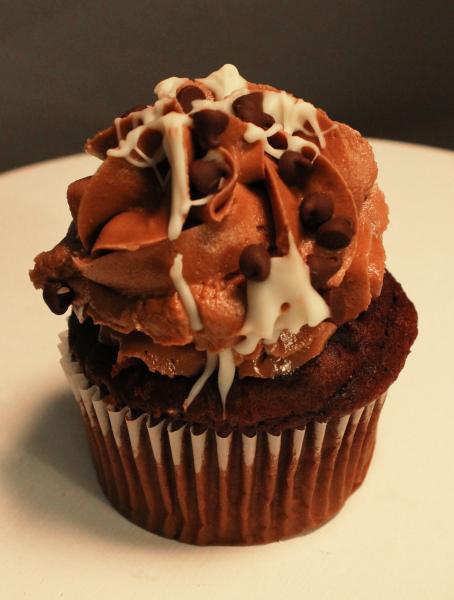 A melt in your mouth chocolate cupcake with chocolate icing, white chocolate drizzled on top with chocolate chips. 